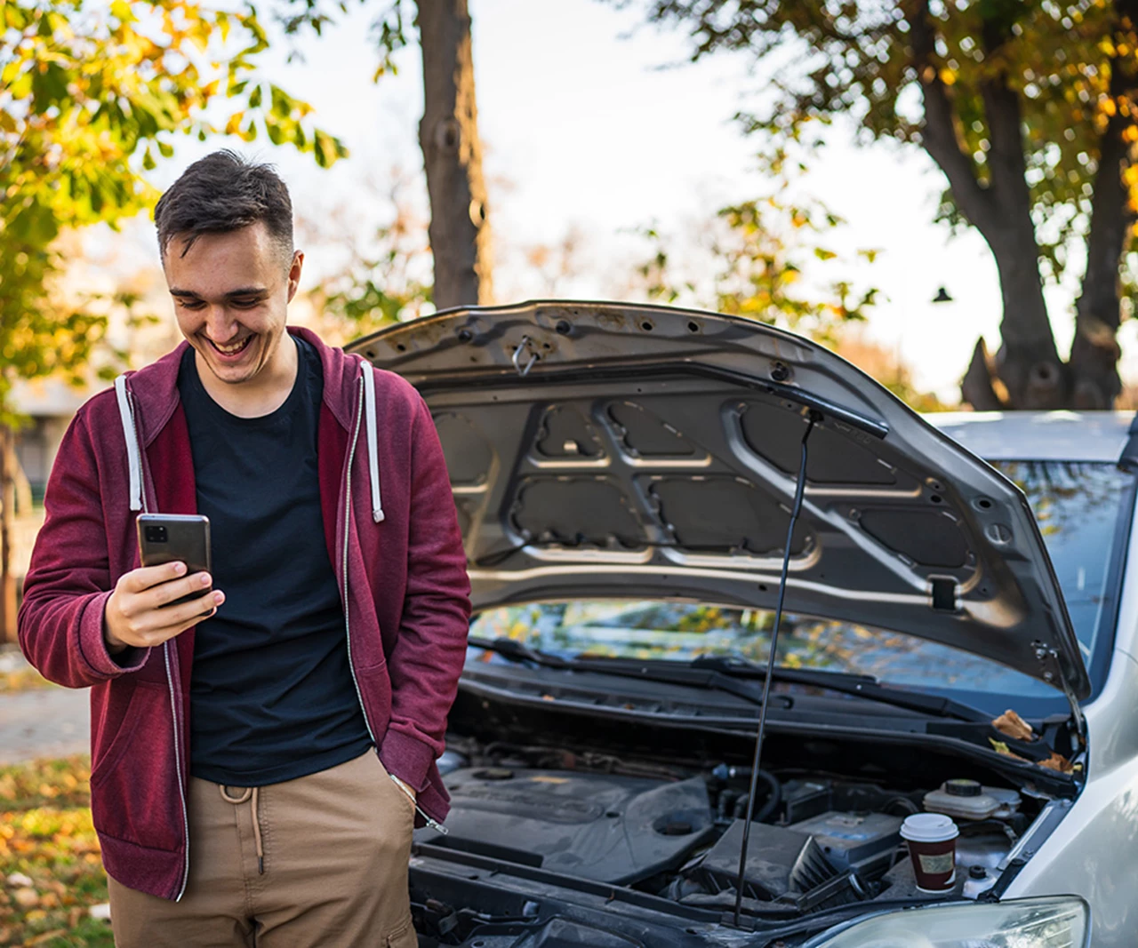 Smiling Man looking at phone in front of disabled car