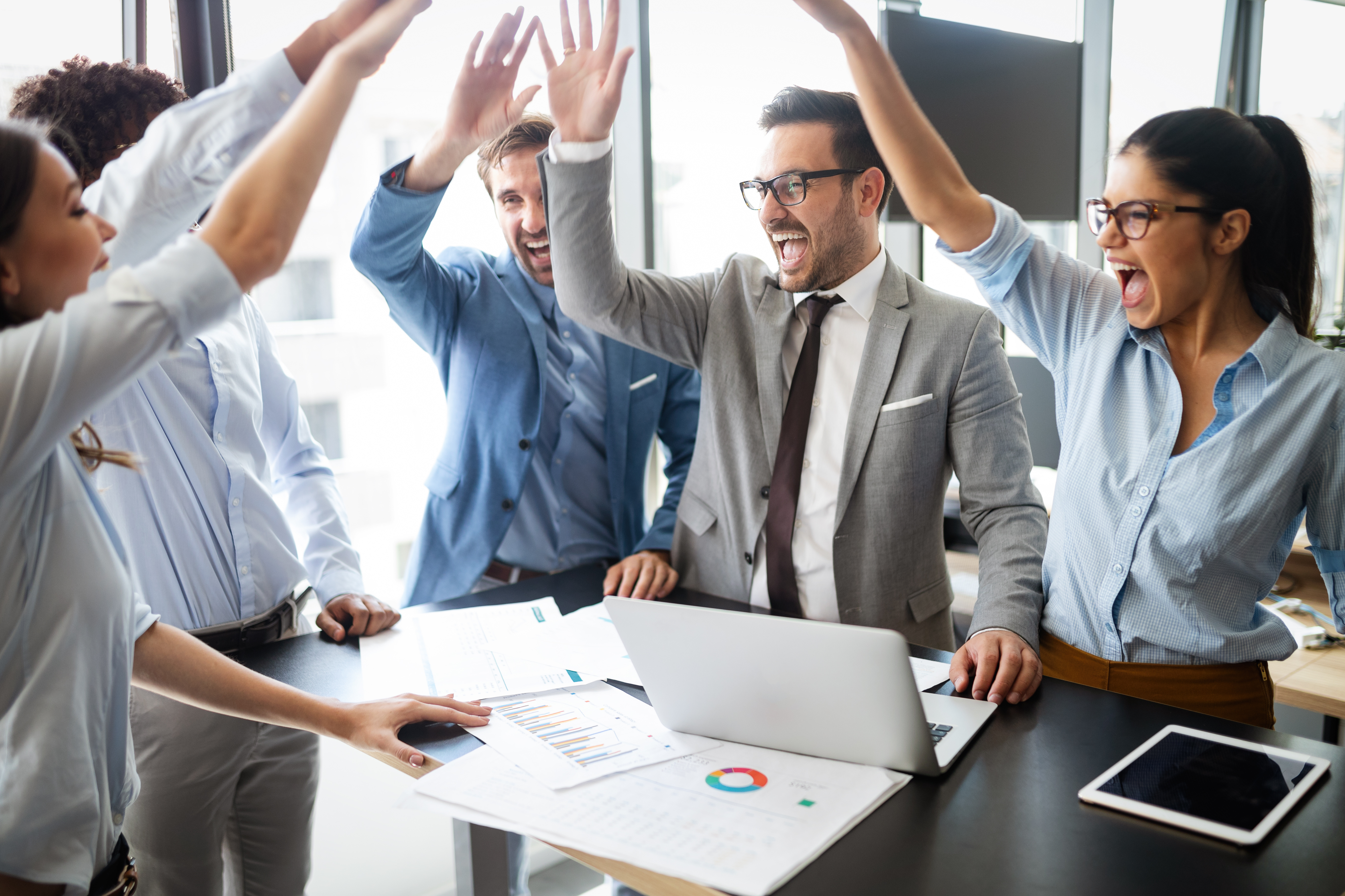 Group of office workers standing around a table high fiving each other