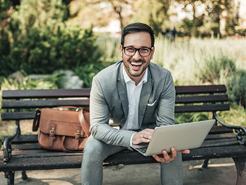 Businessman sitting on a park bench holding a laptop