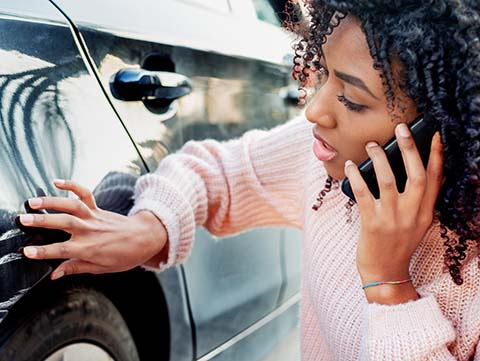 Woman talking on cellphone looking at scrape on car