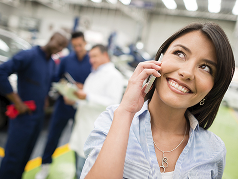 Woman talking on cellphone with auto repair workers in background