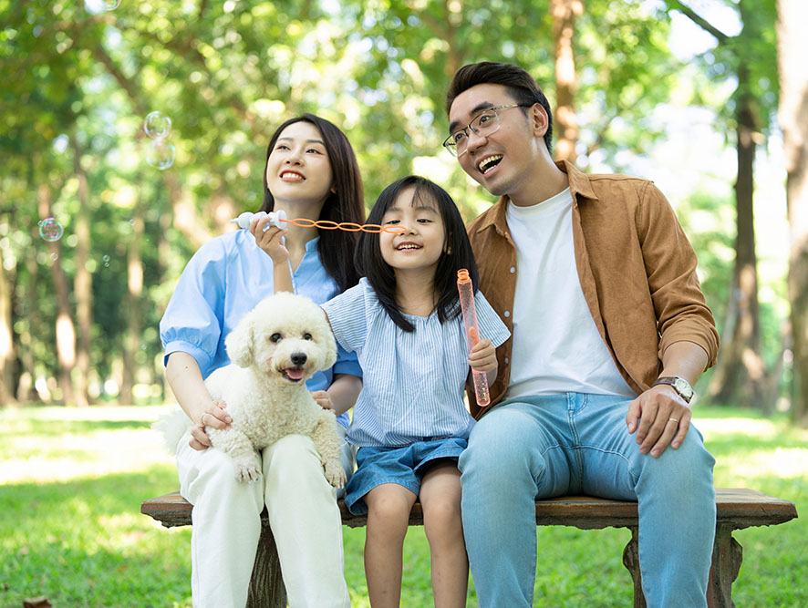 Asian family sitting on park bench with dog