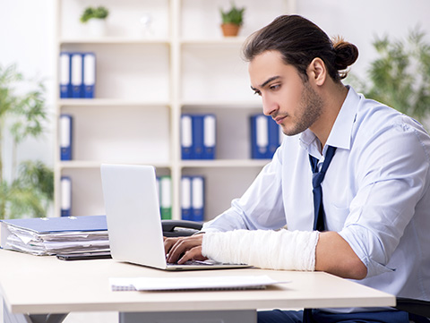 Businessman with arm wrapped in gauze working at laptop