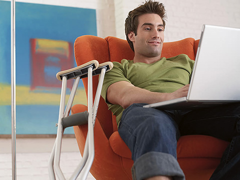 Man sitting in chair with crutches leaning on it, working on laptop