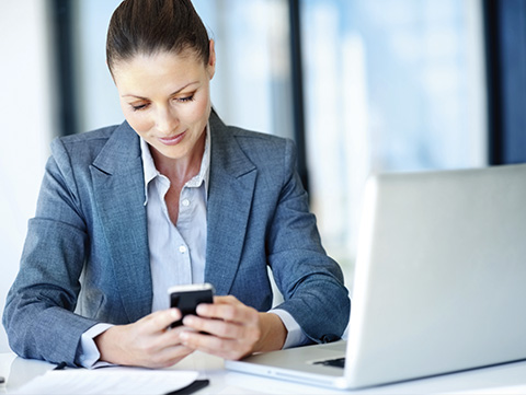 Businesswoman holding cellphone near laptop