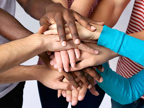 Close up of group of people putting their hands on top of each other's hands