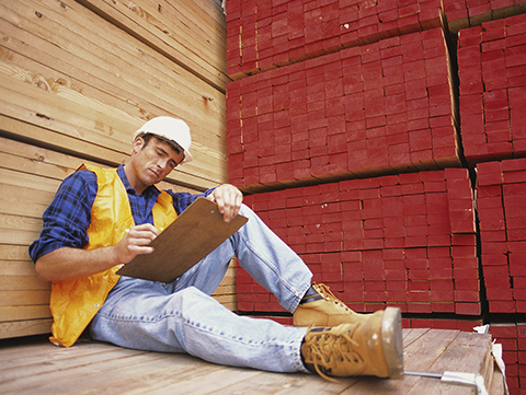 Male construction worker sitting on pile of building materials looking at clipboard