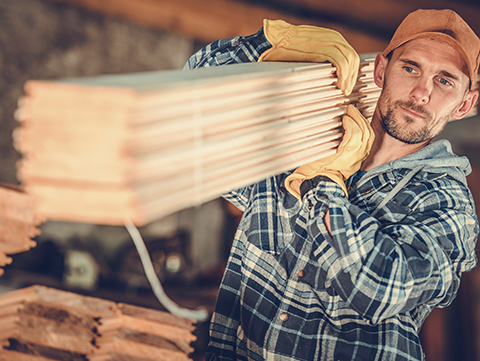 Male contractor carrying building materials on shoulder