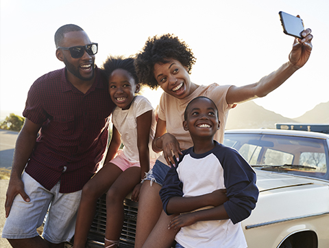 African-American family taking selfie at front of car